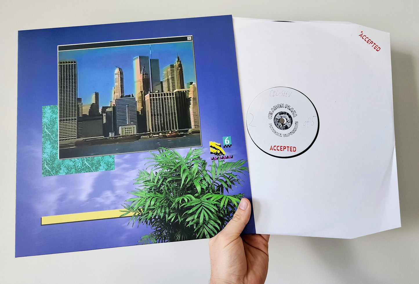 Album cover with cityscape and plant, held open to reveal a VINYL inside.