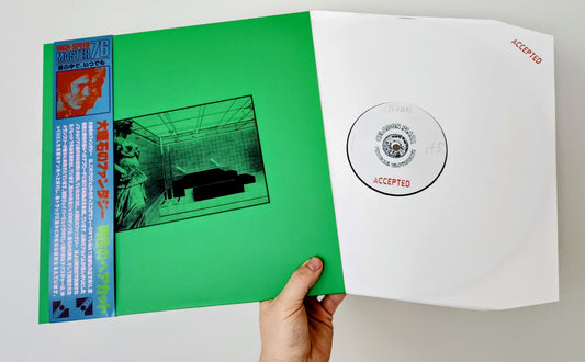 Vinyl record with green cover and white inner sleeve held by a hand on a light gray background